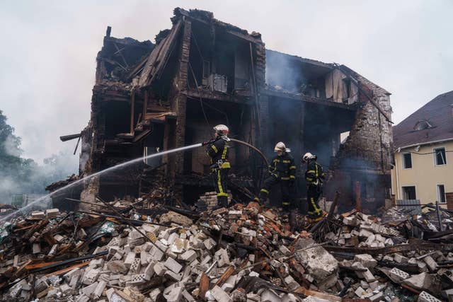 Firefighters tackling fires it the shadow of a completely destroyed and fire-damaged property