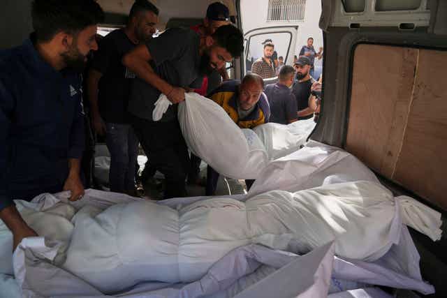 Bodies in white shrouds are put in a vehicle