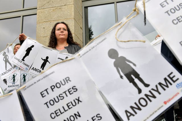 A woman peers behind a banner representing anonymous victims
