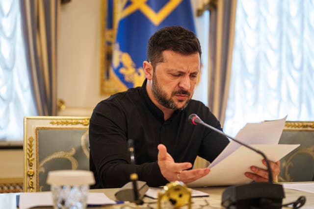 Volodymyr Zelensky at a desk holding paper