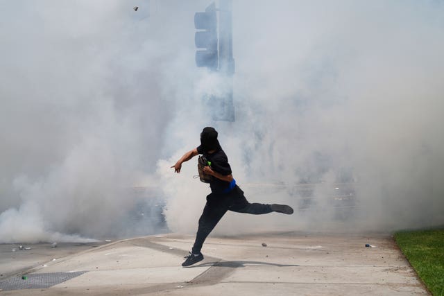 A protester throwing a rock while surrounded by tear gas