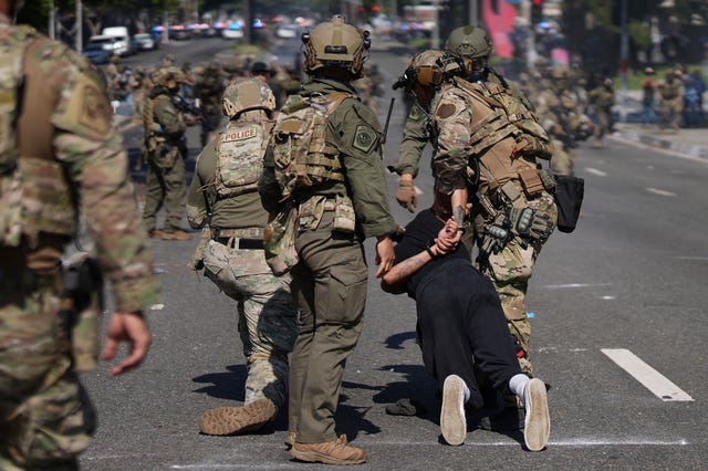 A man is detained, on his knees, by police on a road