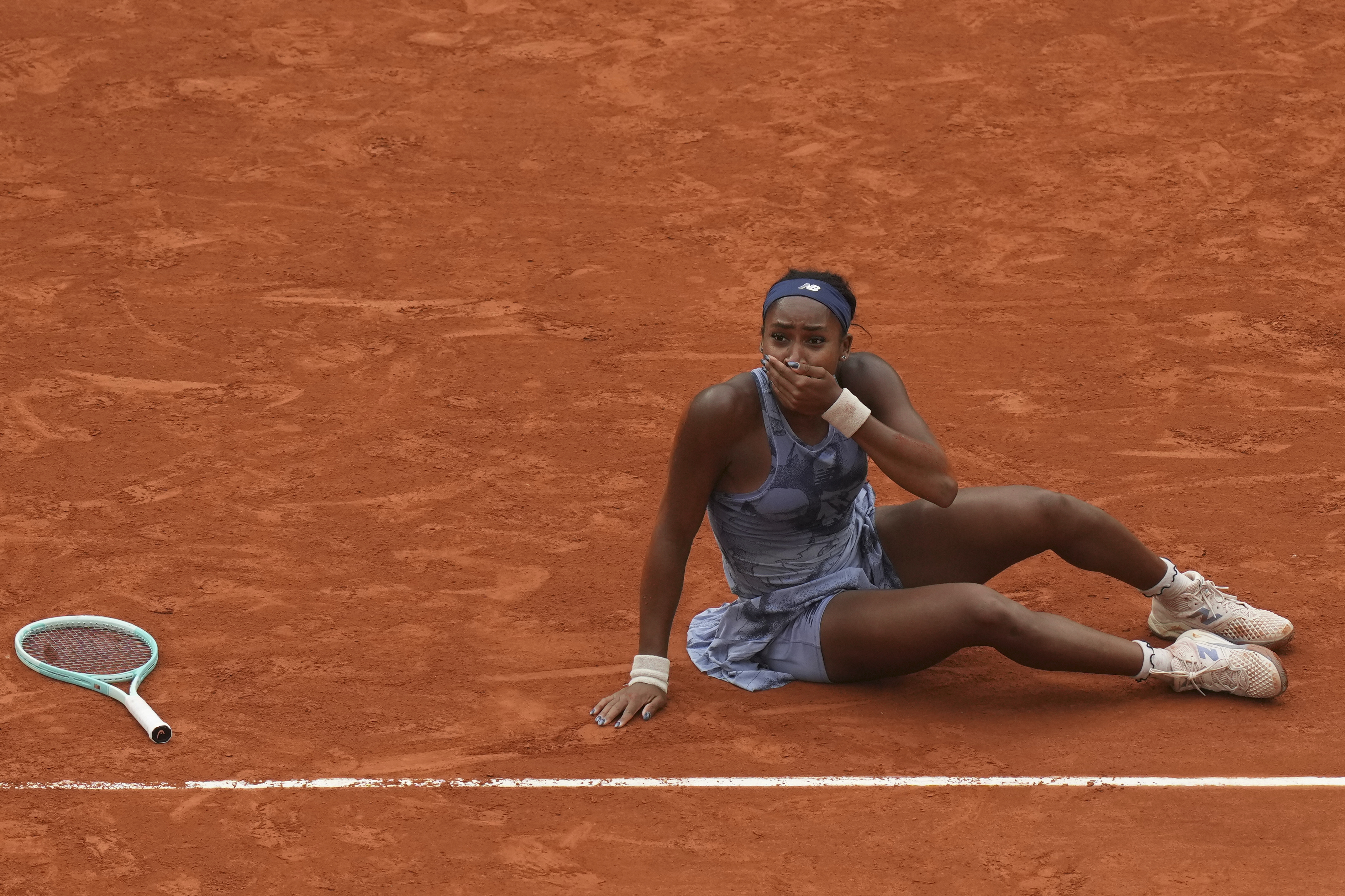 Coco Gauff sits on the clay with her hand over her mouth after winning French Tennis final against Aryna Sabalenka