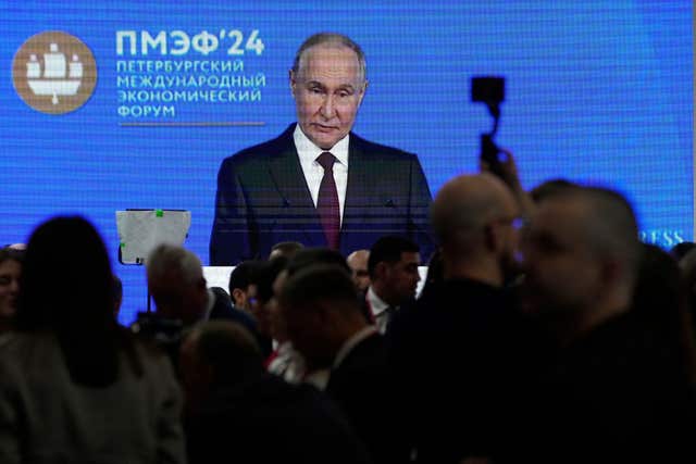 People walk in front of a TV screen showing Russian president Vladimir Putin