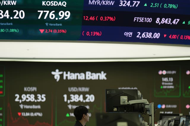 A dealer watches his computer monitors near screens showing stocks information