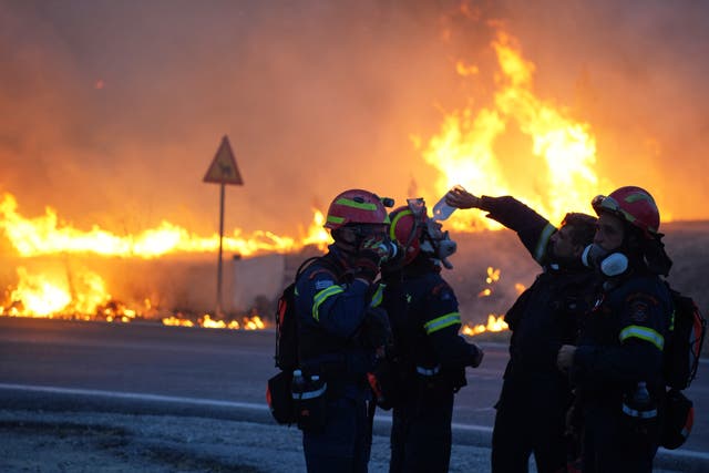 A firefighter pours water to cool down his colleague as they battle a large wildfire on Chios