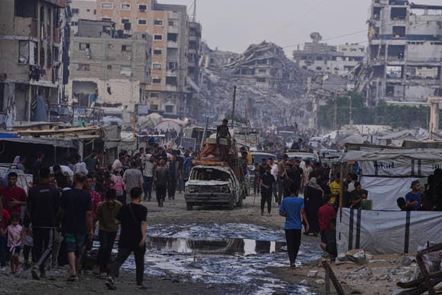 A damaged car carrying furniture and a mattress drives among pedestrians through a market surrounded by destroyed buildings in Gaza City, northern Gaza Strip