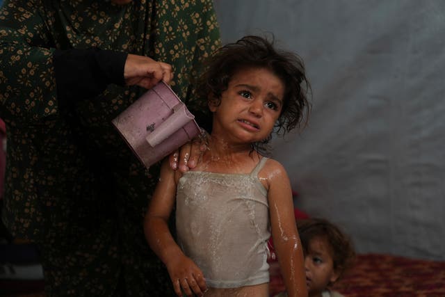 Rida Abu Hadayed, 32, uses water to cool off her two-year-old daughter Azhar inside their tent