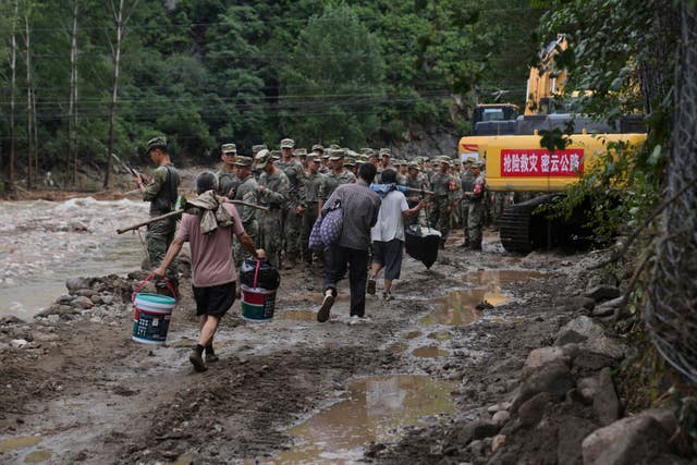 Villagers carrying belongings walk past soldiers heading to rescue trapped villagers on a road damaged by floods after heavy rains in Miyun district on the outskirts of Beijing
