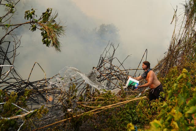 A man throws a bucket of water during a wildfire on the outskirts of Patras, western Greece