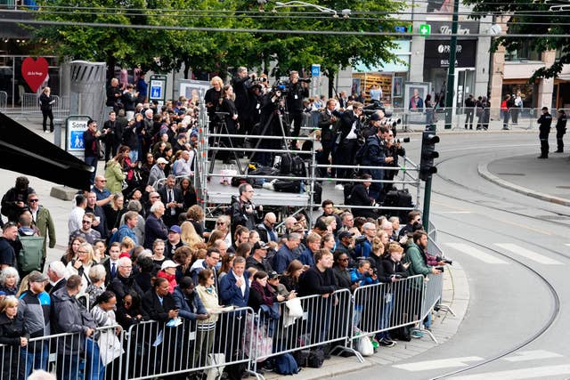 Members of the public wait behind a barrier along the route of the procession