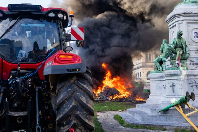 Protesters burn rubbish near a statue and tractor during a demonstration of European farmers near the European Parliament in Brussels