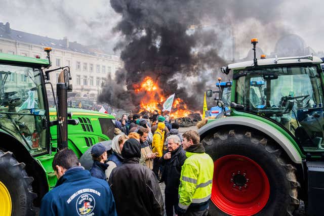 Protesters stand next to tractors as tyres burn during a demonstration of European farmers outside an EU summit meeting in Brussels
