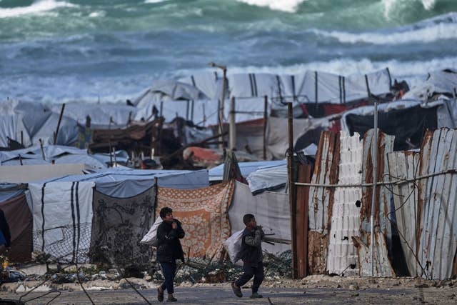 Two children carry items in a makeshift camp on a beach