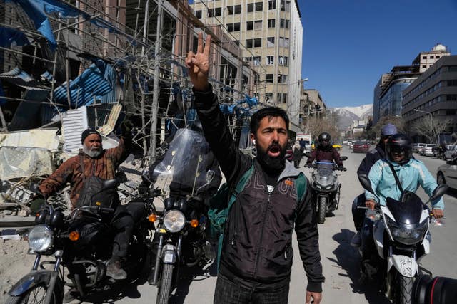 A man shows a victory sign as he chants slogans against the US and Israel in front of a building which was damaged after a strike on a police station amid the US–Israeli military campaign in Tehran, Iran