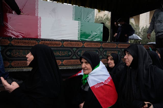 Women follow a truck carrying the flag-draped coffins of Iran’s intelligence minister