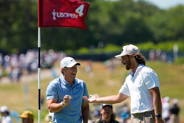 Rory McIlroyhands a ball to Tommy Fleetwood standing behind a flag