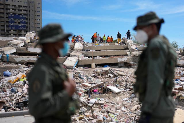 National Guard troops stand guard as rescue workers search through the rubble of a building destroyed by the earthquakes