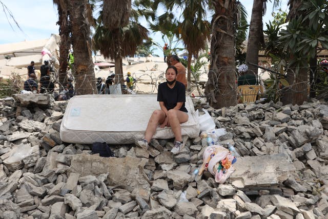 A woman sits in the rubble next to her home destroyed by the earthquakes