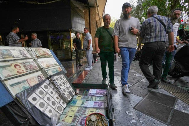 Pedestrians walk past a pavement display of Iranian currency and vintage banknotes and coins in Tehran