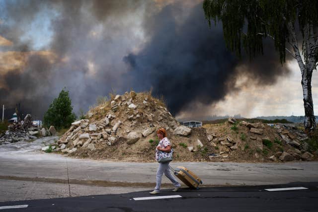 A woman walks along a road as smoke rises from a destroyed warehouse after a Russian drone attack on the outskirts of Kyiv, Ukraine