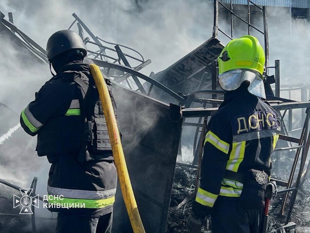 The backs of two firefighters tackle a blaze, with smoke rising in front of them
