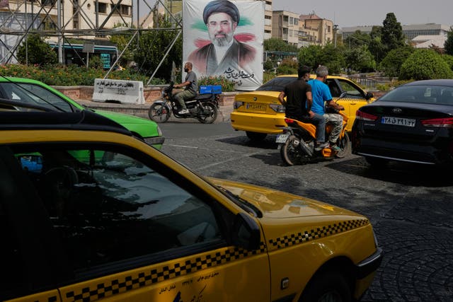 Vehicles pass a banner showing a portrait of the Iranian Supreme Leader Ayatollah Mojtaba Khamenei in Tehran