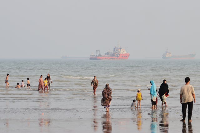 People at a beach as commercial vessels are anchored in the Strait of Hormuz