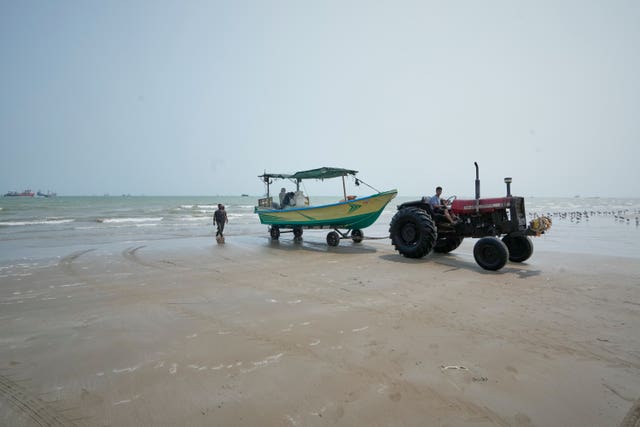 A tractor pulls a motorboat from the water onto the beach next to the Strait of Hormuz