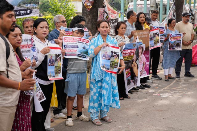 Relatives of recent flash flood victims hold banners urging authorities to step up efforts to find their missing loved ones
