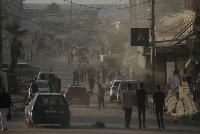 People and cars travel along a road, surrounded by war-damaged buildings