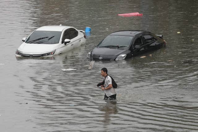 A man wades through water with half-submerged cars behind him