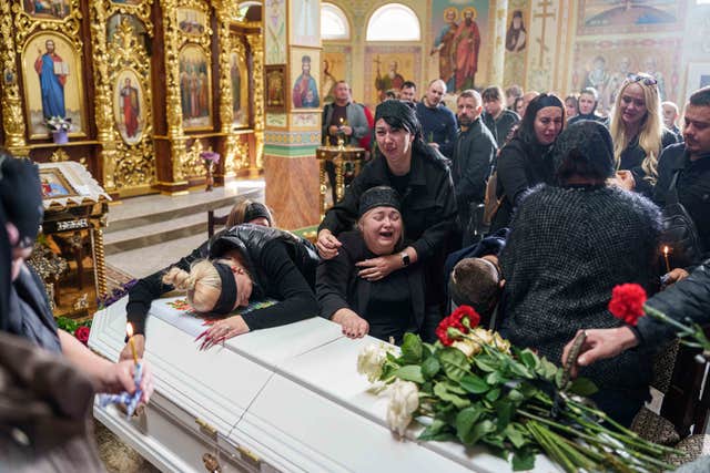 A mother surrounded by family cries sitting by the coffin of her son Illia Honcharenko, 14, killed by a Russian rocket strike on a residential house
