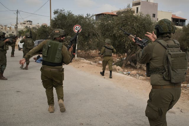 Israeli soldiers move toward a Palestinian man lying wounded on a road