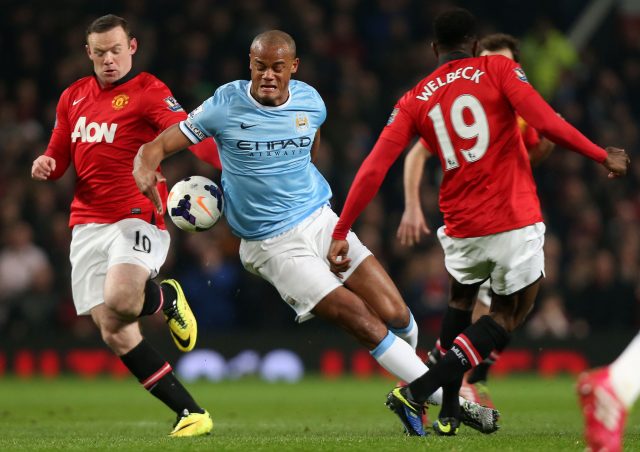 Manchester City's Vincent Kompany, centre, battles for the ball with Manchester United's Wayne Rooney (Peter Byrne/PA)
