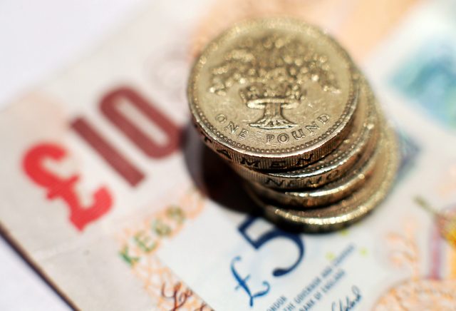 A pile of one pound coins placed on five pound and ten pound banknotes