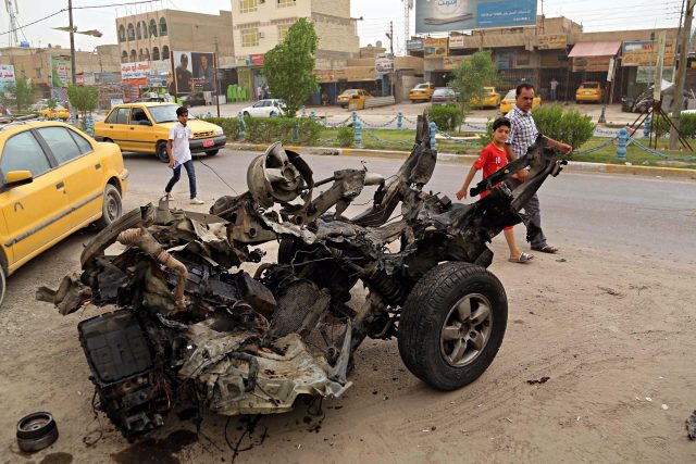 Civilians pass a destroyed car in the a car bomb explosion in southwestern Baghdad, Iraq