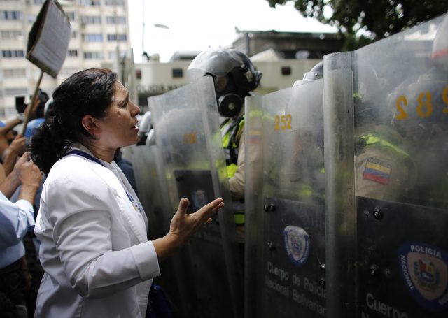 A woman confronts a line of police officers in riot gear during an anti-government protest in Caracas (Ariana Cubillos/AP)