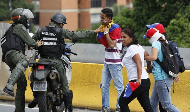 A Bolivarian National Guard briefly tries to remove the flag around the neck of a protester before letting him go, after security forces blocked an opposition march from reaching the National Electoral Council headquarters in Caracas (Ariana Cubillos/AP)