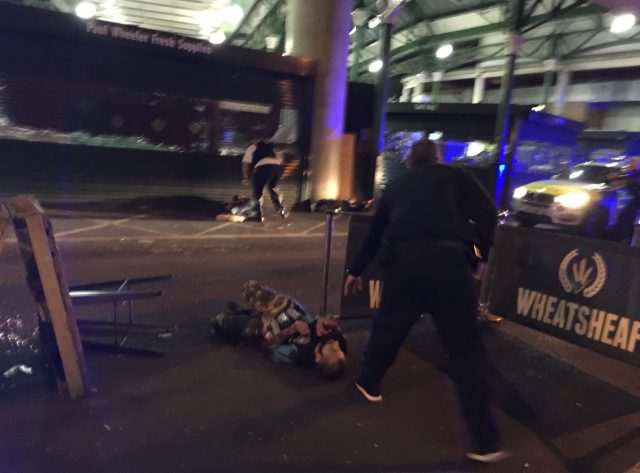 This photo taken by Gabriele Sciotto shows a man, foreground, one of the suspects, wearing what appear to be canisters strapped to his chest lying on the ground after being shot by police outside Borough Market (Gabriele Sciotto via AP)