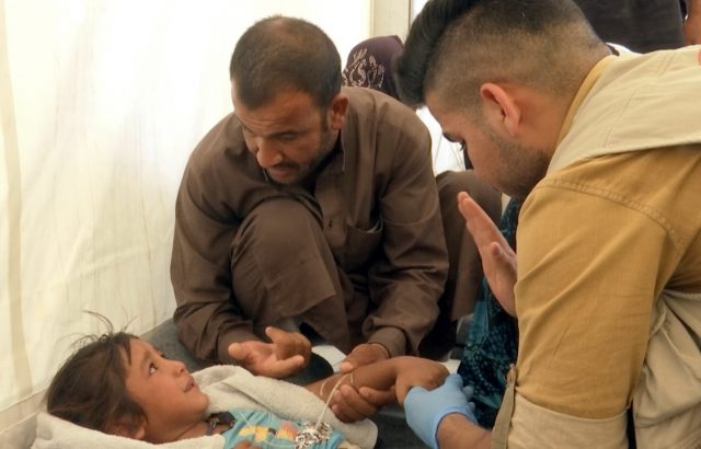 In this frame grab from video, a man comforts his daughter as a doctor treats her after she was taken ill with suspected food poisoning in the Hassan Sham U2 camp (Balint Szlanko/AP)