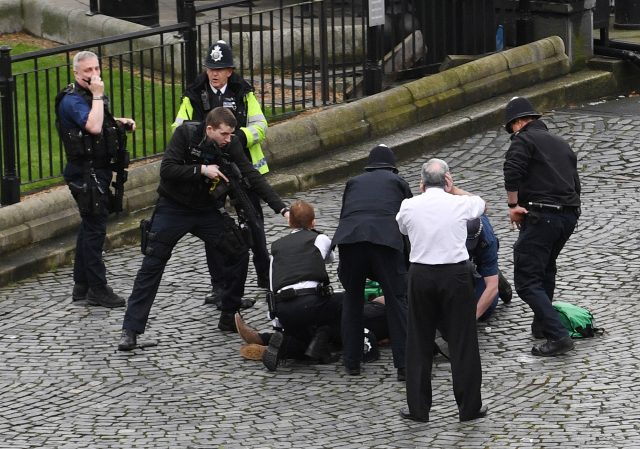 A policeman points a gun at a Khalid Masood on the floor as emergency services attend the scene outside the Palace of Westminster, 