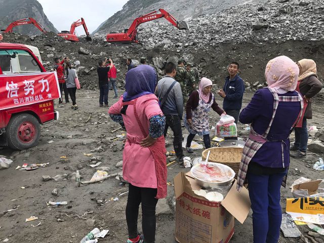 Women watch as earthmoving equipment digs at the site of a landslide in Xinmo village in Maoxian County in southwestern China's Sichuan Province (Ng Han Guan/AP)