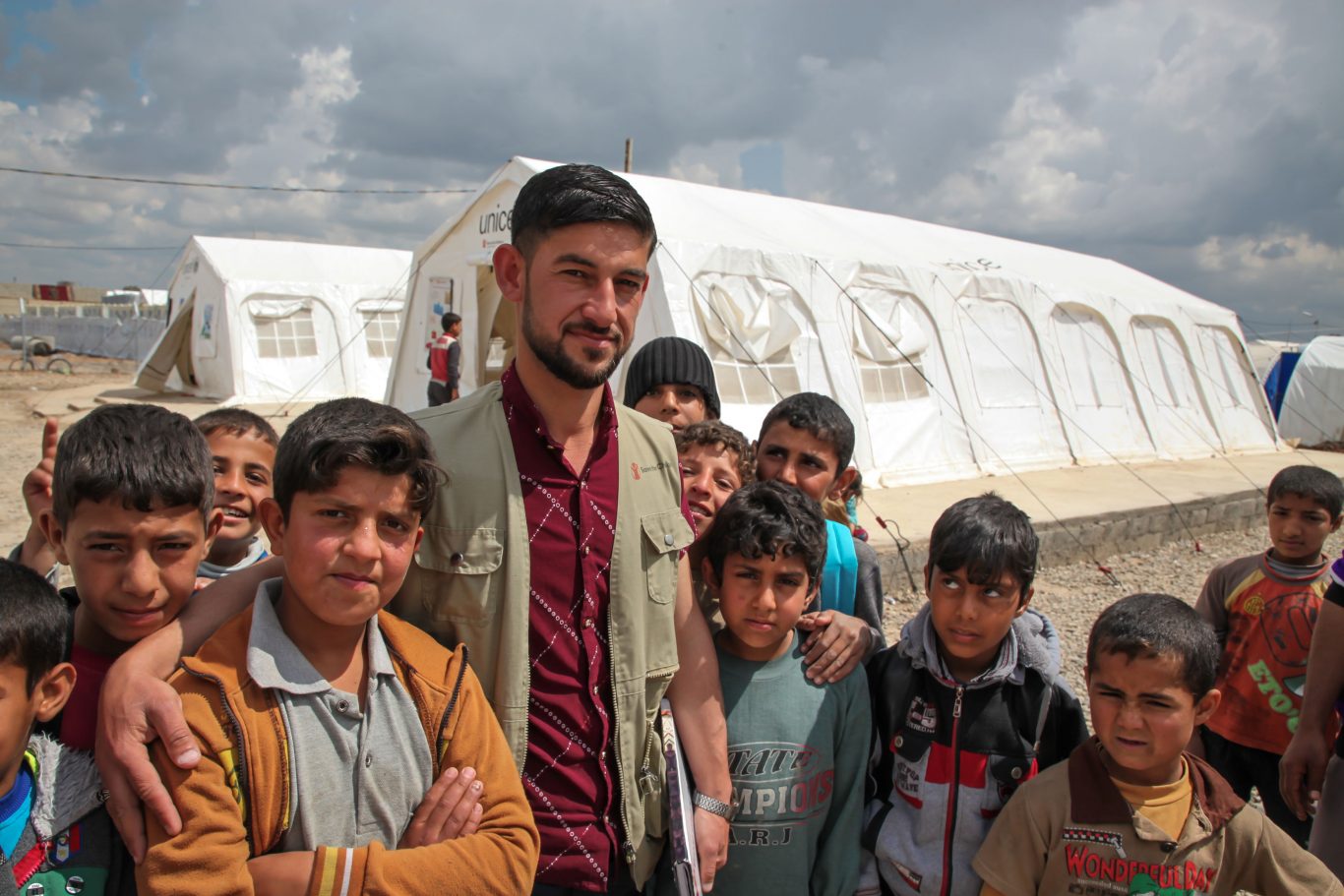 Riyadh, one of Save the Children's Community Mobilisers, stands with children at Hamam Al Ali Camp (Save The Children)