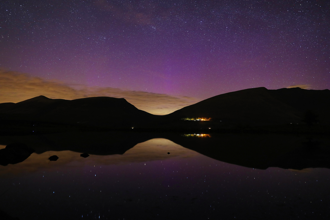 A purple sky caused by the Northern lights know as the Aurora Borealis reflected in Tewet Tarn with the famous Blencathra mountain