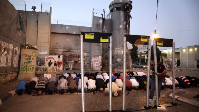 Palestinians pray in front of mock metal detectors during a demonstration in Bethlehem
