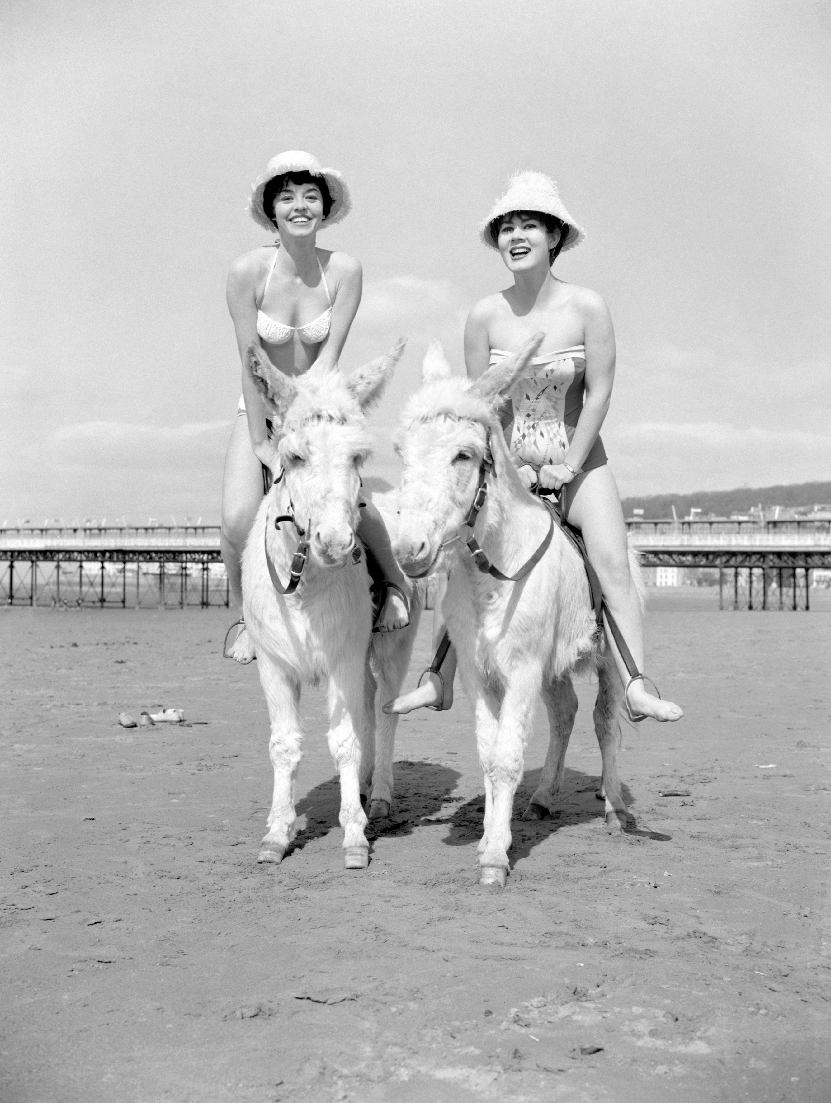 Windmill girls riding white donkeys across the beach