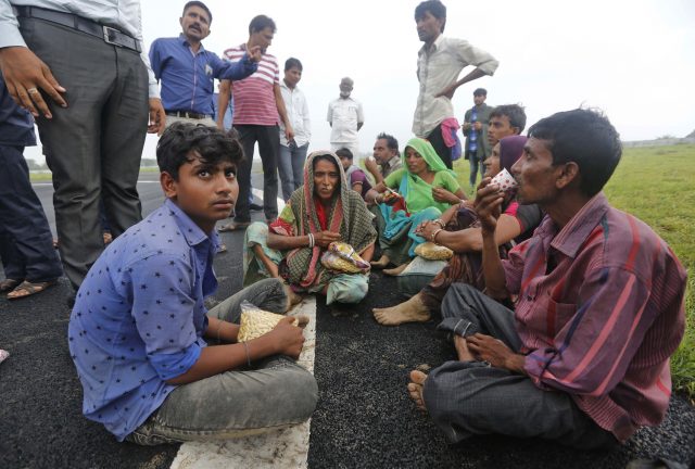 Indian flood victims who were air-lifted in an air force helicopter sit at an airport in Deesa, Gujarat (Ajit Solanki/AP/PA)