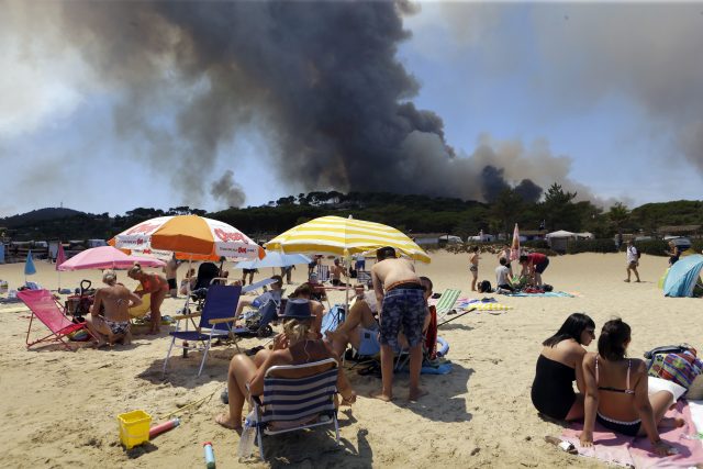 People enjoy sunbathing on the beach in Lavandou, French Riviera, as plumes of smoke rise in the air from burning wildfires  (Claude Paris/AP)
