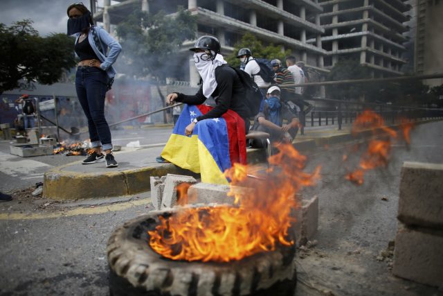 Masked anti-government demonstrators stand next to a burning tyre in Caracas (Ariana Cubillos/AP)